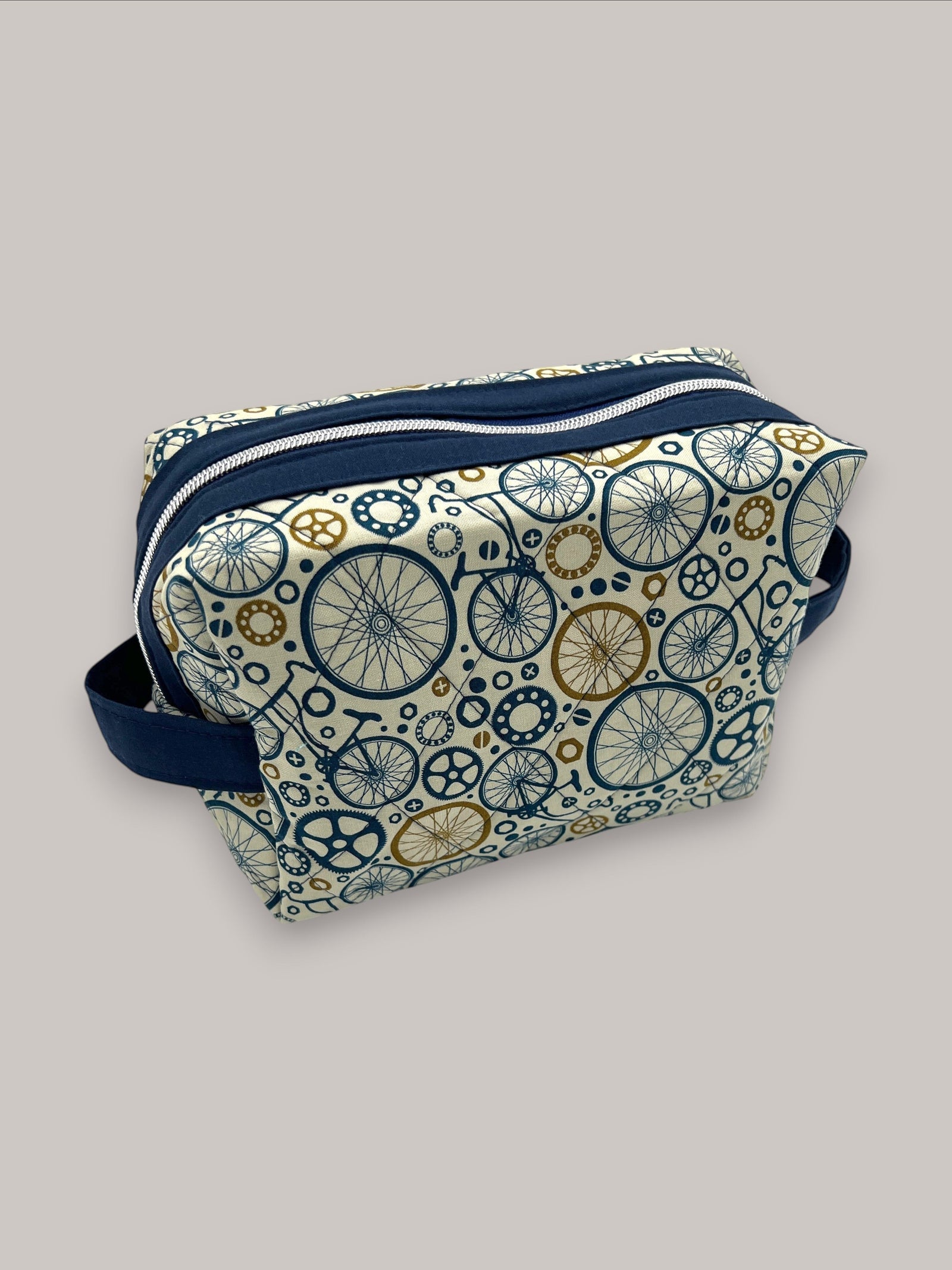 Wheels Go Round Holland pouch in cream with a navy and gold bicycle-wheel print, front three-quarter view, zipped closed — handmade by The Cozy Daisy