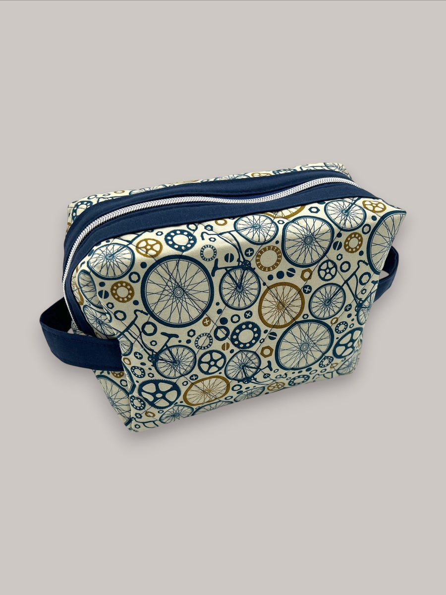 Wheels Go Round Holland pouch in cream with a navy and gold bicycle-wheel print, front three-quarter view, zipped closed — handmade by The Cozy Daisy